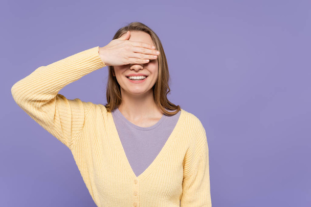 glückliche junge Frau bedeckt Augen isoliert auf lila - Foto, Bild