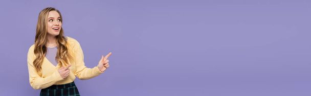 joyful young woman pointing with fingers isolated on purple, banner - Foto, Bild