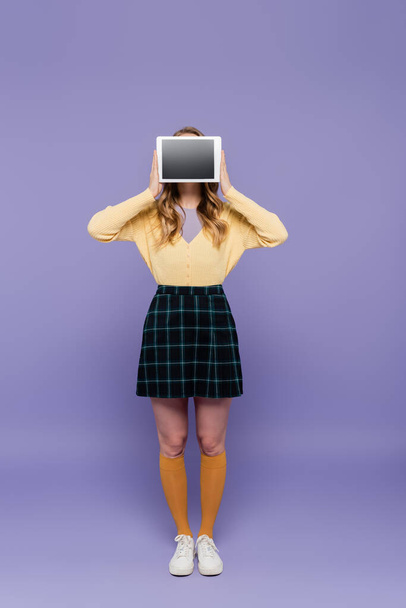 young woman covering face while holding digital tablet with blank screen on purple - Zdjęcie, obraz