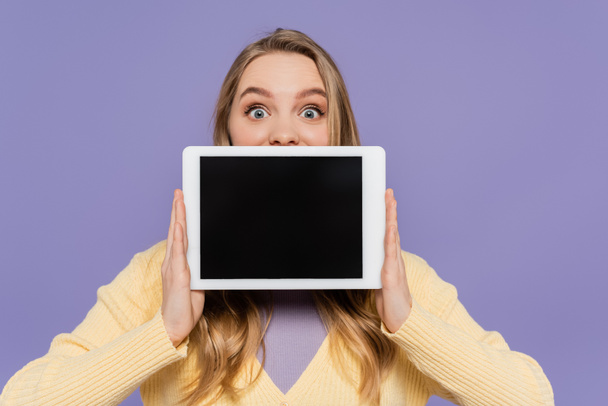 young woman covering mouth and holding digital tablet with blank screen isolated on purple - 写真・画像