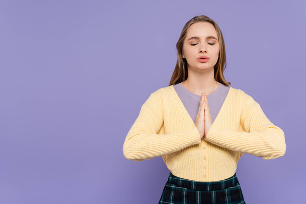молода жінка з закритими очима і молитовними руками ізольована на фіолетовому
 - Фото, зображення