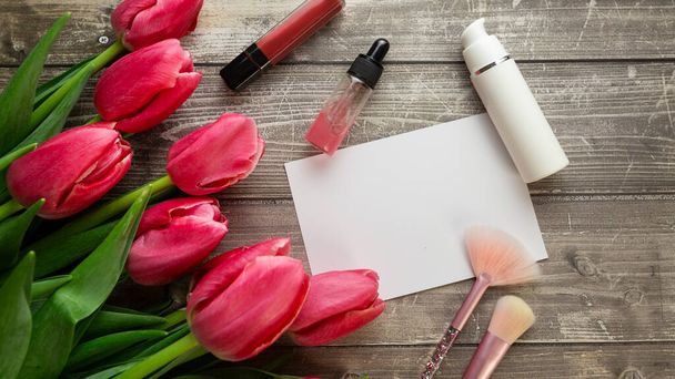 Scrivania da lavoro femminile con cosmetici, rossetto e fiori di tulipano su fondo in legno. Posa piatta, vista dall'alto - Foto, immagini
