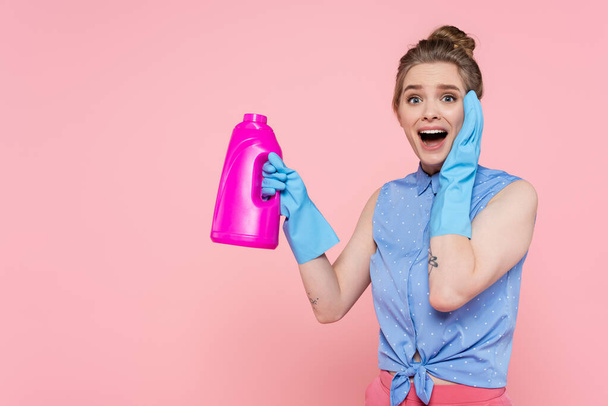 excited young woman in rubber gloves holding bright bottle with detergent isolated on pink  - Fotó, kép