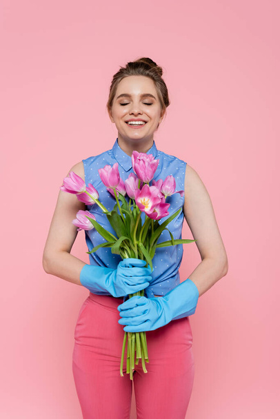 happy young woman in rubber gloves holding tulips isolated on pink - Zdjęcie, obraz
