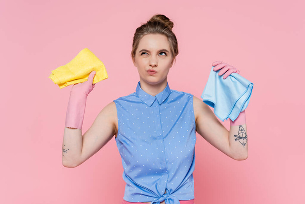 ゴム手袋の若い女性がピンクに隔離された青と黄色のラグを保持  - 写真・画像