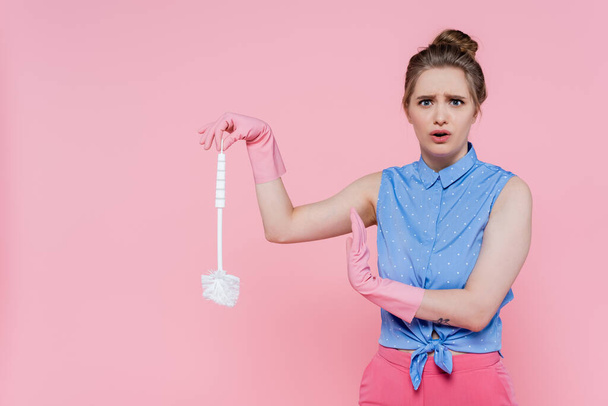 tattooed young woman in rubber gloves holding toilet brush isolated on pink  - Foto, afbeelding