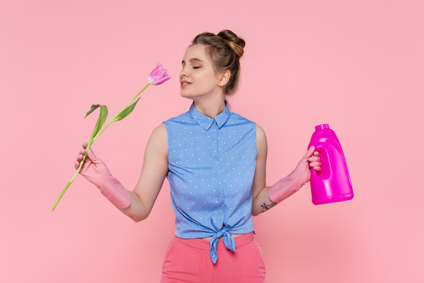 young woman holding bottle with detergent and smelling tulip isolated on pink  - Fotografie, Obrázek