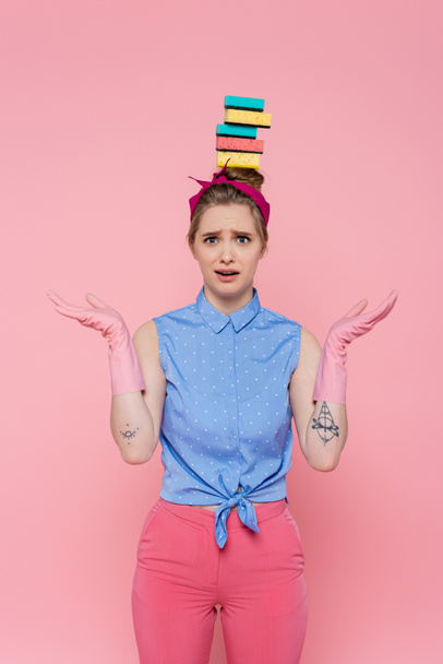 confused young woman with stacked sponges on head isolated on pink  - Фото, изображение