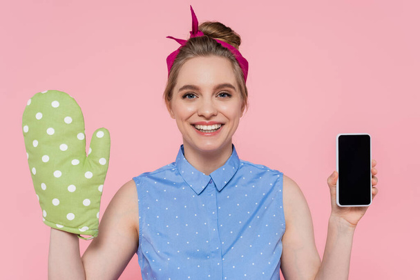 happy young woman with green baking glove holding smartphone with blank screen isolated on pink - Fotografie, Obrázek