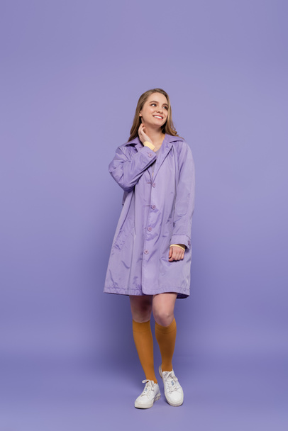 full length of happy young woman in violet rain coat standing on purple - Foto, Imagem