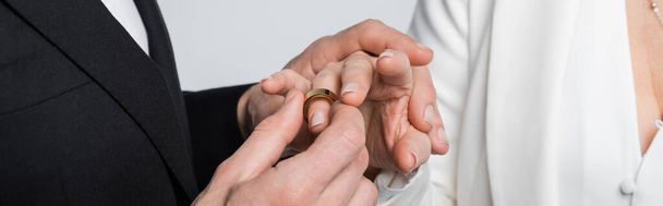 Cropped view of groom wearing wedding ring on finger of bride isolated on grey, banner  - Φωτογραφία, εικόνα