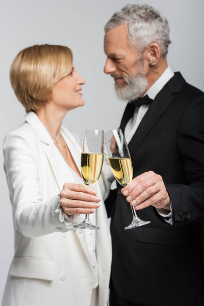 Side view of blurred mature couple in wedding clothes clinking champagne isolated on grey  - Foto, Bild