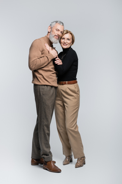 Stylish mature couple looking at camera and hugging on grey background  - Foto, Imagem