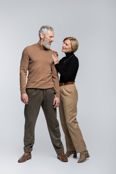 Blonde woman touching stylish mature husband on grey background  - Foto, imagen