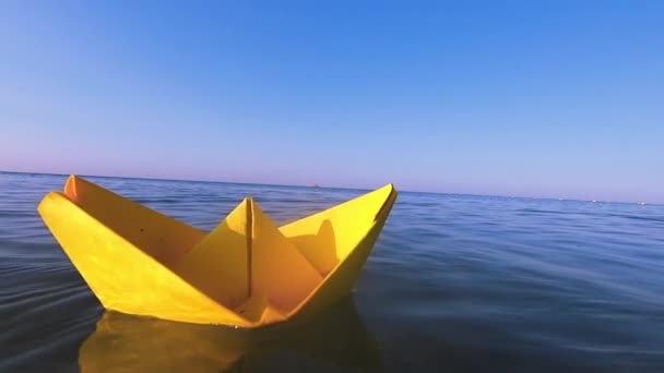 Bateau en papier jaune flotte à la surface des vagues d'eau bleue de la mer gros plan. - Séquence, vidéo