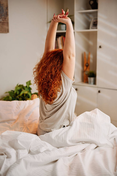 Una ragazza rossa si sveglia al mattino e tende le braccia. - Foto, immagini