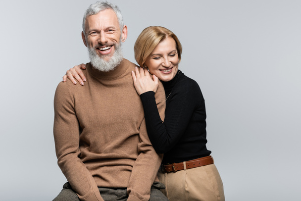 Blonde woman in turtleneck hugging mature husband isolated on grey  - Photo, Image