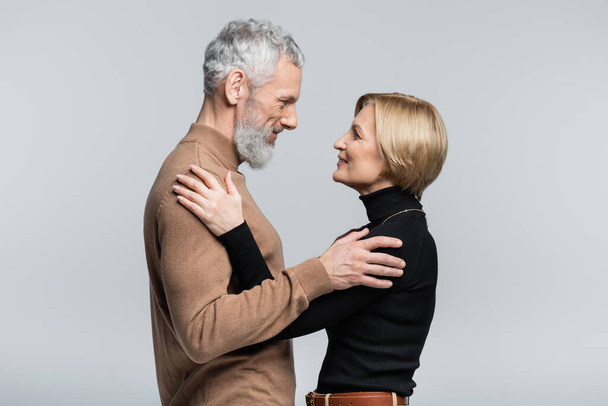 Side view of positive mature couple hugging isolated on grey  - Fotografie, Obrázek