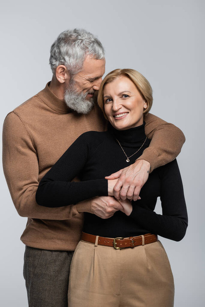 Grey haired man in turtleneck embracing blonde wife isolated on grey  - Fotoğraf, Görsel
