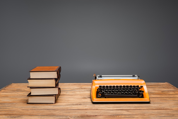 máquina de escribir naranja y pila de libros en escritorio de madera aislado en gris - Foto, Imagen