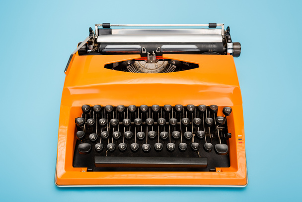bright orange typewriter with black keyboard on blue background - Foto, Imagen