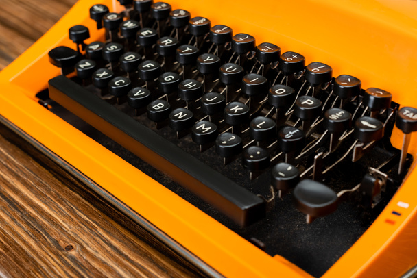 vista de cerca del teclado negro de la máquina de escribir naranja en la superficie de madera - Foto, Imagen