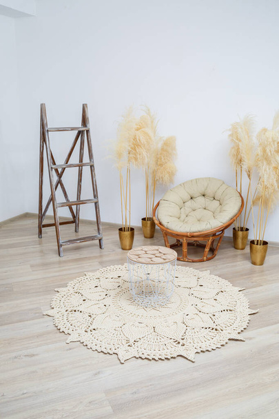 太い糸で作られた手作りの手編みのラグ:ベージュ糸で作られた手作りのラグは、アームチェアの近くのリビングルームにあり、編み物の芸術 - 写真・画像