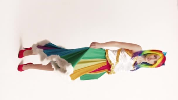 Vertical Studio Shot coqueta joven mujer toca sus clavículas después de girar alrededor en pura falda de arco iris fondo blanco - Imágenes, Vídeo