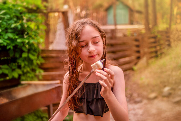 Tiener meisje rust en eten. Meisje eet marmellou gekookt op een kampvuur op een zomerdag. - Foto, afbeelding