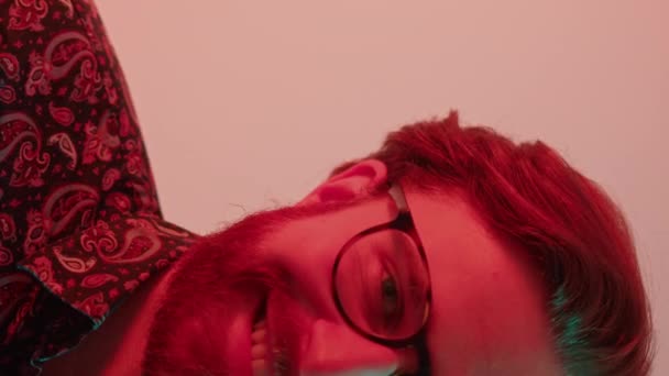 félarcú jóképű Y-generációs fiatalember arcszőrzet visel szemüveget és mosolyog a kamera függőleges közeli stúdió lövés - Felvétel, videó