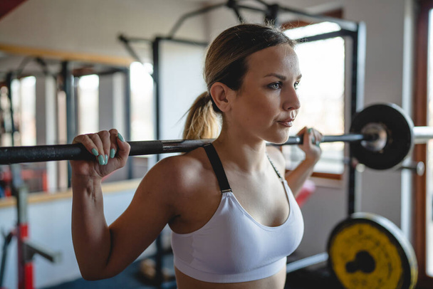 One woman training at gym female athlete doing squats with barbell and weight on her shoulders close up copy space strength and fitness exercise concept - Photo, Image