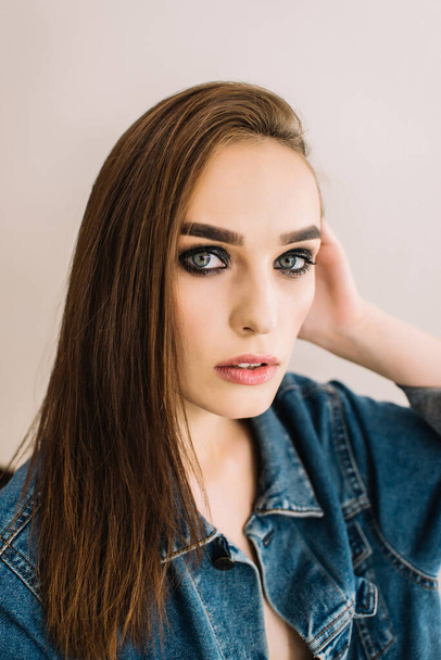 Brunette girl wearing denim jacket and looking at camera. Bright evening makeup, smoky eyes, close up portrait - Foto, afbeelding