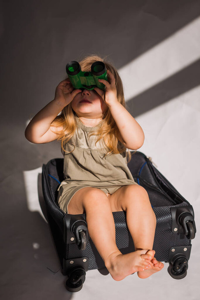 girl looking on binoculars, feeling unhappy, sitting on suitcase - Photo, image