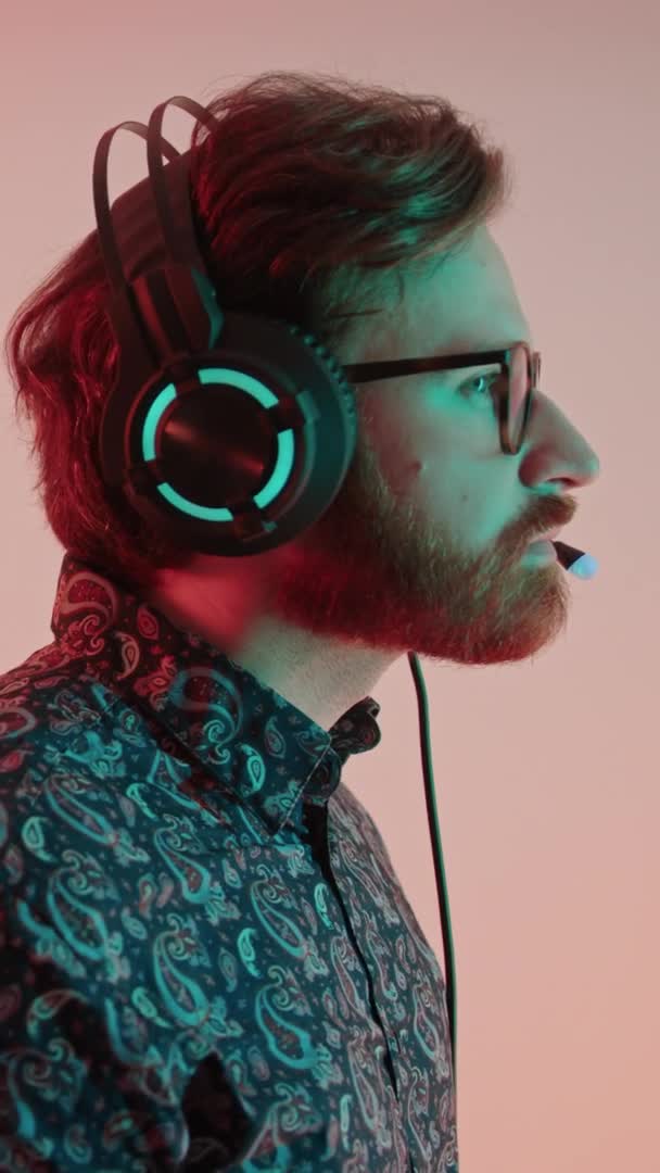 profilo colpo millenario caucasico barbuto gamer in una camicia fantasia con la luce del computer sul suo viso verticale colpo in studio - Filmati, video