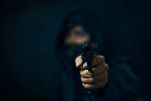 Uomo in cappuccio e maschera minaccia con arma da fuoco. - Foto, immagini