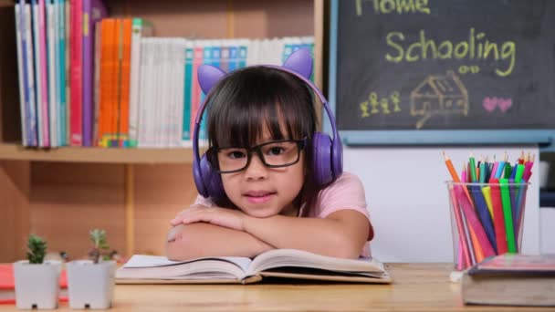 Linda niña con auriculares escuchando audiolibros con libros de aprendizaje en inglés sobre la mesa. Aprender inglés y educación moderna - Metraje, vídeo