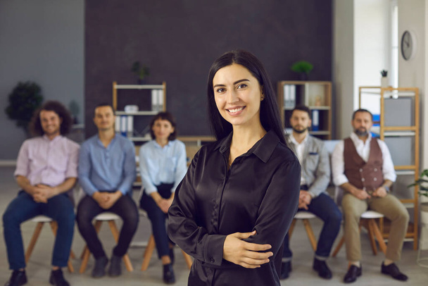 Портрет счастливой молодой предпринимательницы, стоящей перед командой коллег или сотрудников - Фото, изображение
