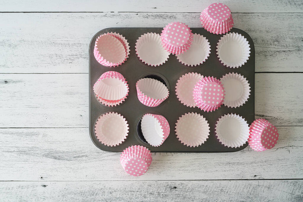 Kupa muffin serpenyő rózsaszín papír bélés közel világos fa háttér, lapos feküdt másolási hellyel - Fotó, kép