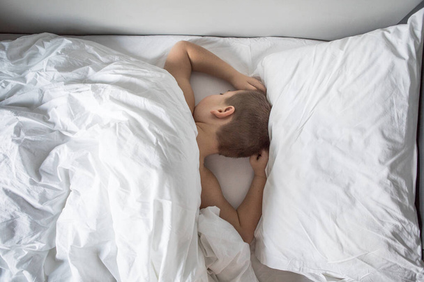 Παιδί 7 χρονών ξαπλωμένο στο κρεβάτι, κοιμισμένο παιδί ξυπνά το πρωί στο δωμάτιο του με πρωινό φως - Φωτογραφία, εικόνα