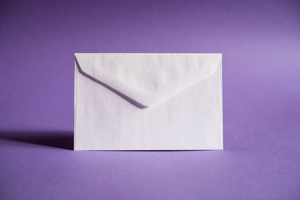 een witte envelop op een paarse achtergrond, stuur een bericht of een nieuwsbericht. - Foto, afbeelding