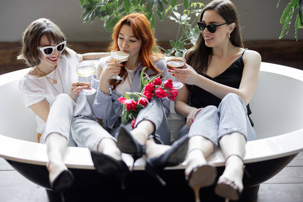 Tři mladé dospělé přítelkyně sedí spolu s alkoholickými nápoji ve vaně - Fotografie, Obrázek