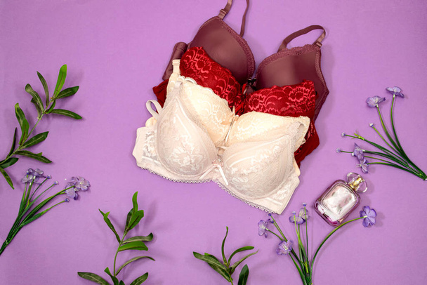  soutien-gorge élégant en dentelle, flacon de parfum et fleurs sur fond violet. Élégante lingerie plat lay - Photo, image
