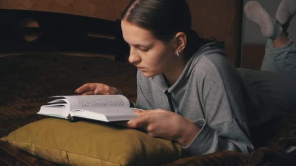 Cute dziewczyna czyta i liści poprzez książkę leżąc wygodnie w łóżku - Materiał filmowy, wideo