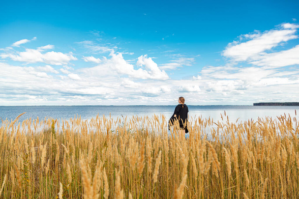 schönes Mädchen in einem Feld am Ufer des Meeres und blauem Himmel mit Wolken aus nächster Nähe - Foto, Bild