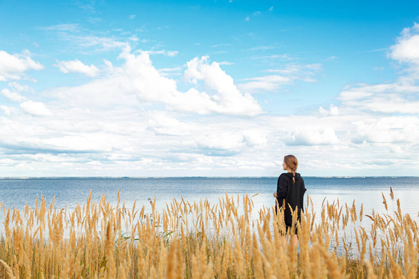 belle fille dans un champ sur le rivage de la mer et ciel bleu avec nuages gros plan - Photo, image
