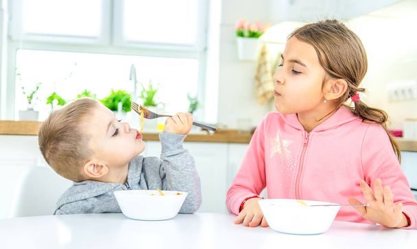 children in the kitchen at the table eat pasta. selective focus - 写真・画像