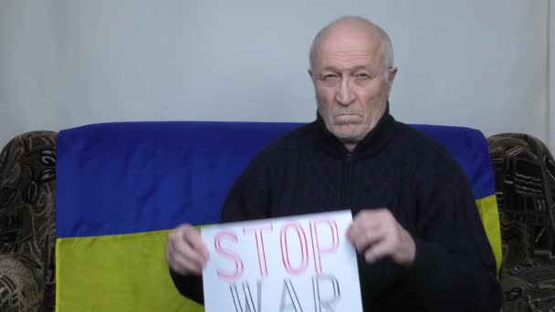Starszy mężczyzna na tle ukraińskiej flagi podnosi znak wojny Stop - Materiał filmowy, wideo