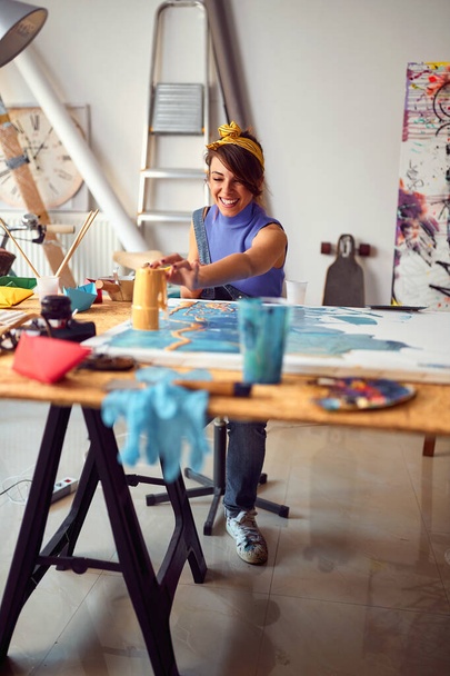 Smiling female artist sitting at desk with painting accessories - Fotoğraf, Görsel