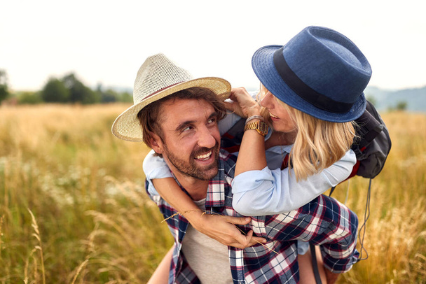 Young couple in field. Smiling Caucasian couple looking at each other and smiling. Girl piggybacking.  Sport, love, freedom, holiday concept. - Photo, image