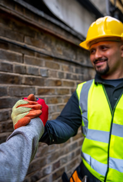 Yakışıklı, mutlu, gülümseyen bir inşaat işçisi meslektaşıyla el sıkışıyor.. - Fotoğraf, Görsel